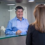Male patient at reception desk speaking with female receptionist in professional office setting