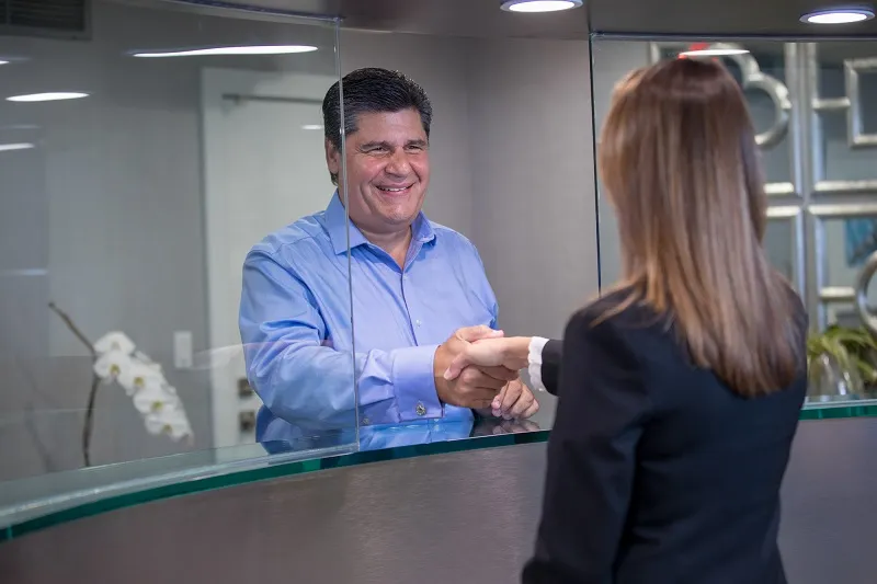 Male patient shaking hands with receptionist at front desk, demonstrating friendly customer service